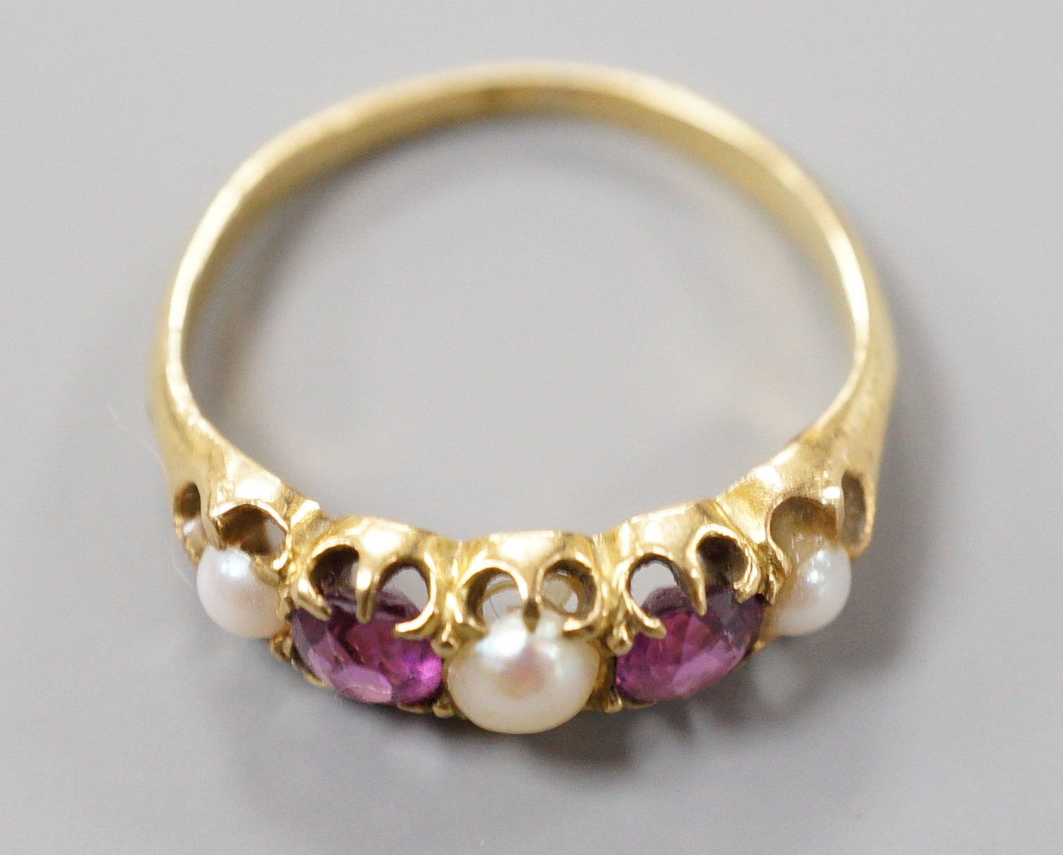 A yellow metal two stone garnet, three stone split pearl set half hoop ring, size K, gross 2.4 grams.